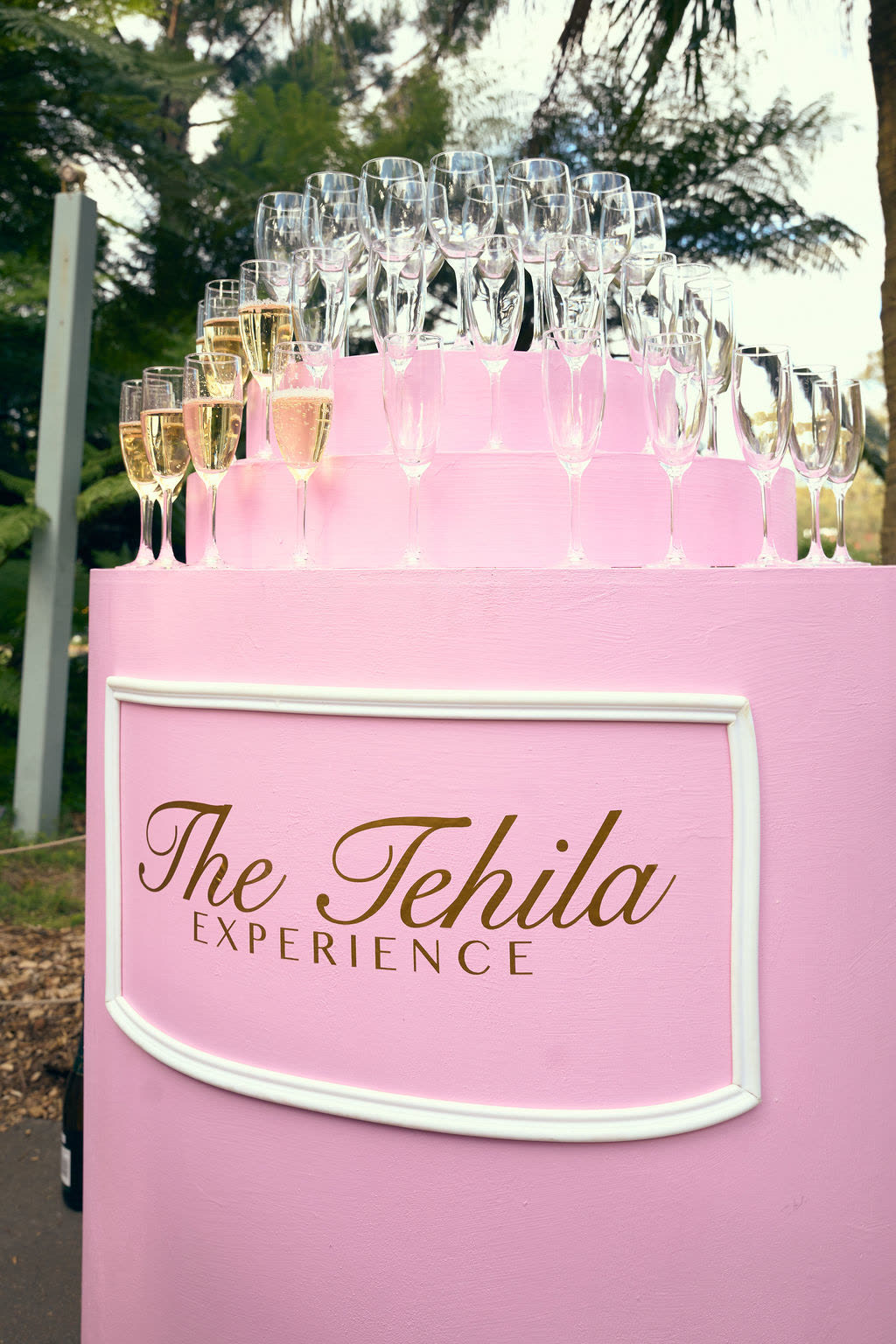 Front of a round pink stand with a tiered top for champagne glasses and a front panel for custom decal lettering
