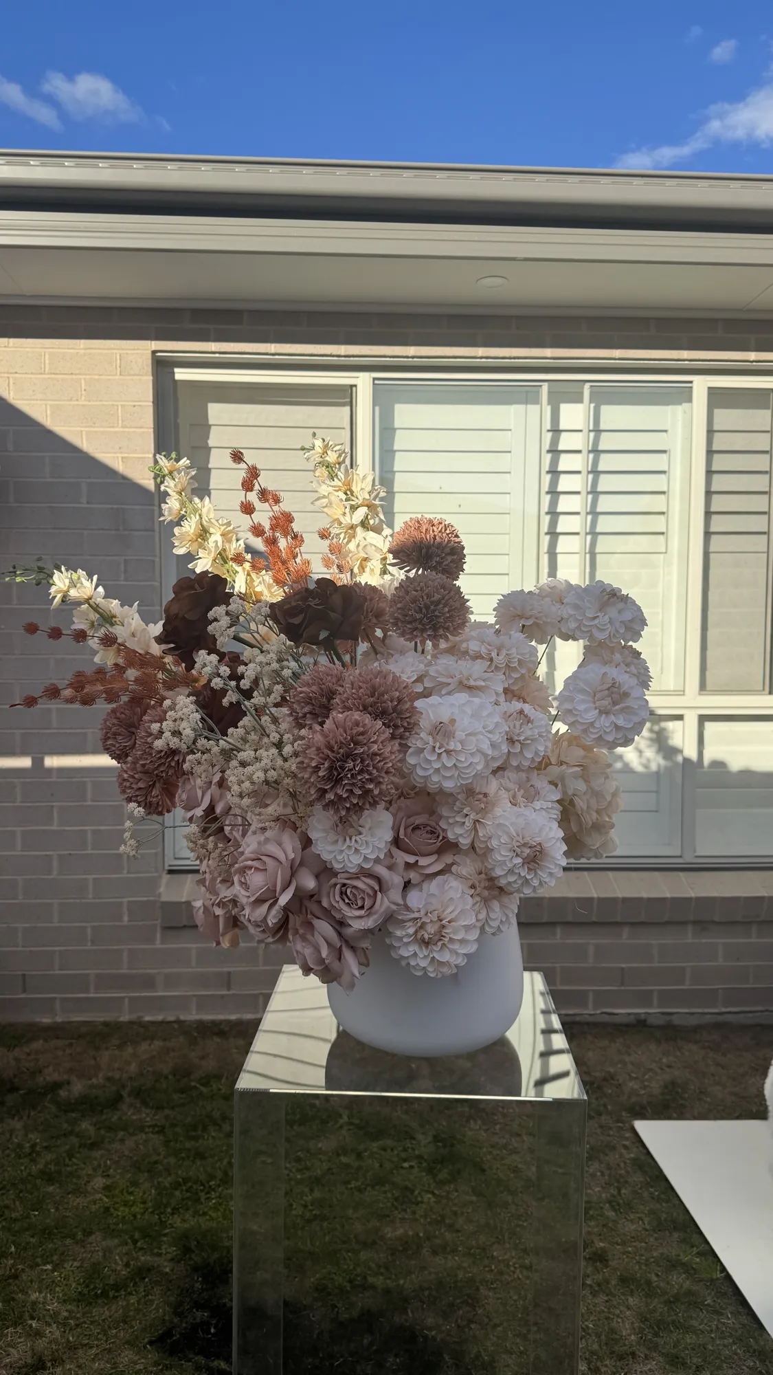 White, pink, and blue flowers with trailing greenery on a clear acrylic plinth.