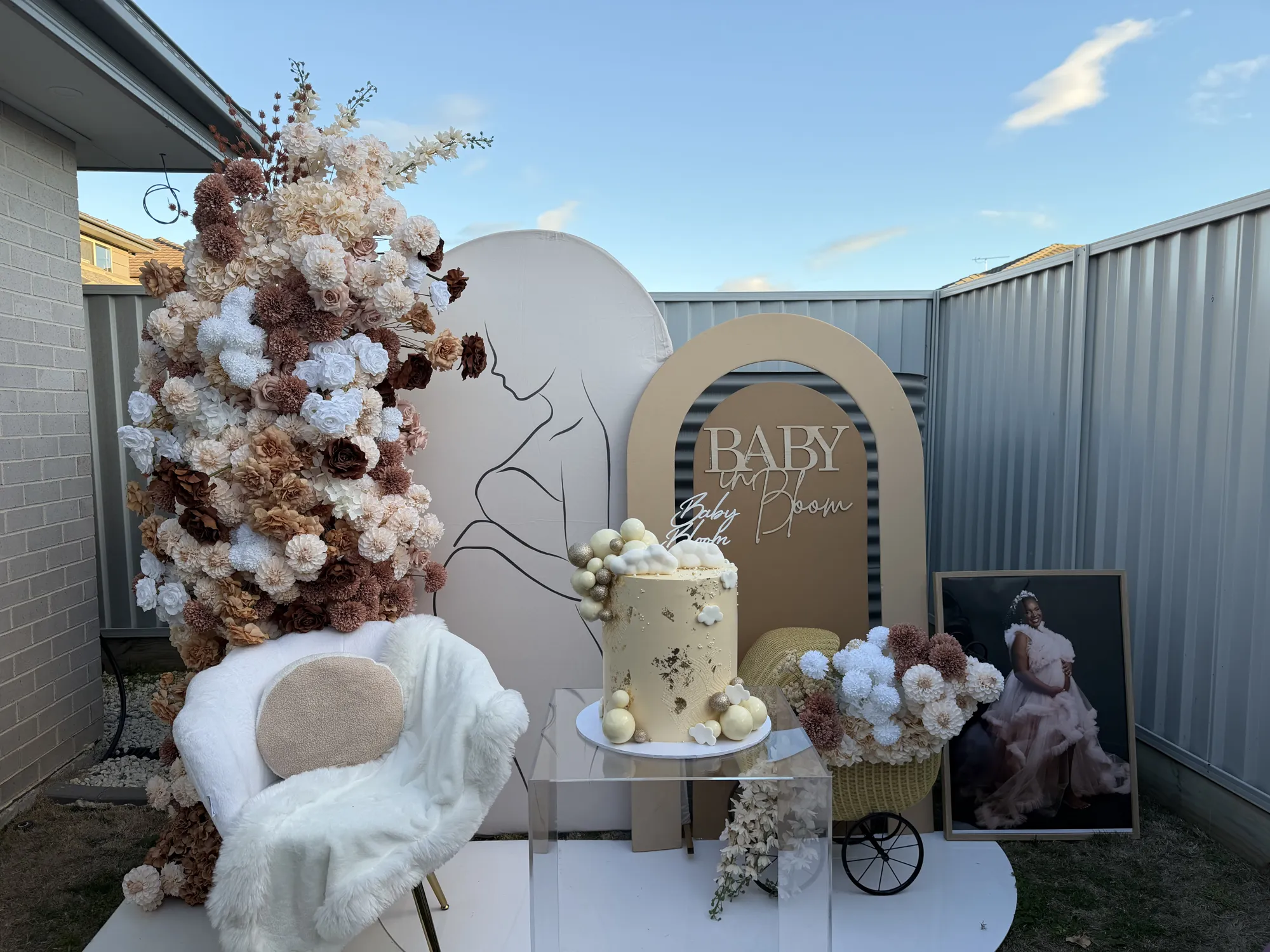 Round tables in white linen with white rose and hydrangea centrepieces, facing a baby shower backdrop and a teddy bear arch.
