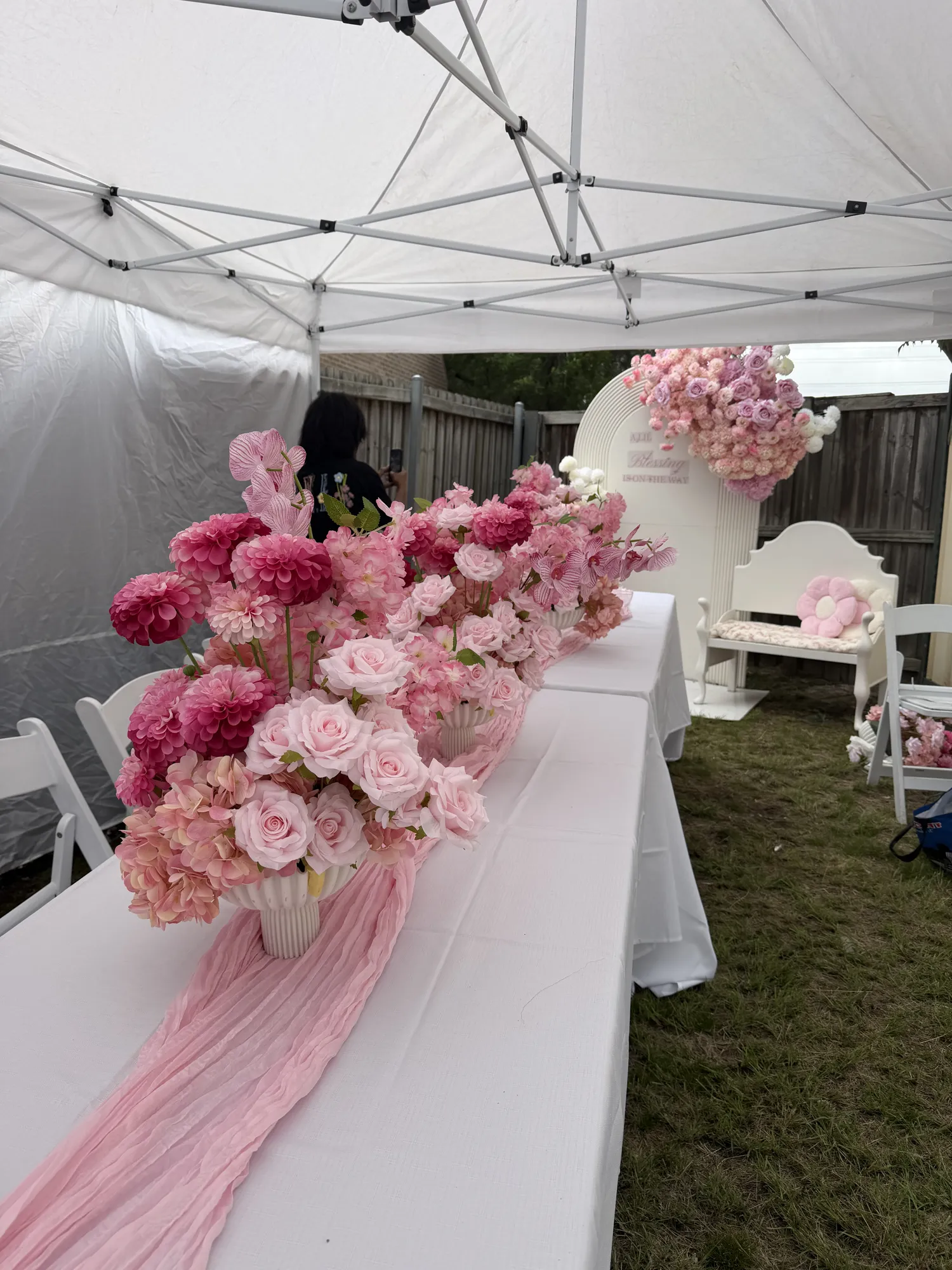 A white welcome sign trimmed with white flowers, beside a flower-trimmed pram.