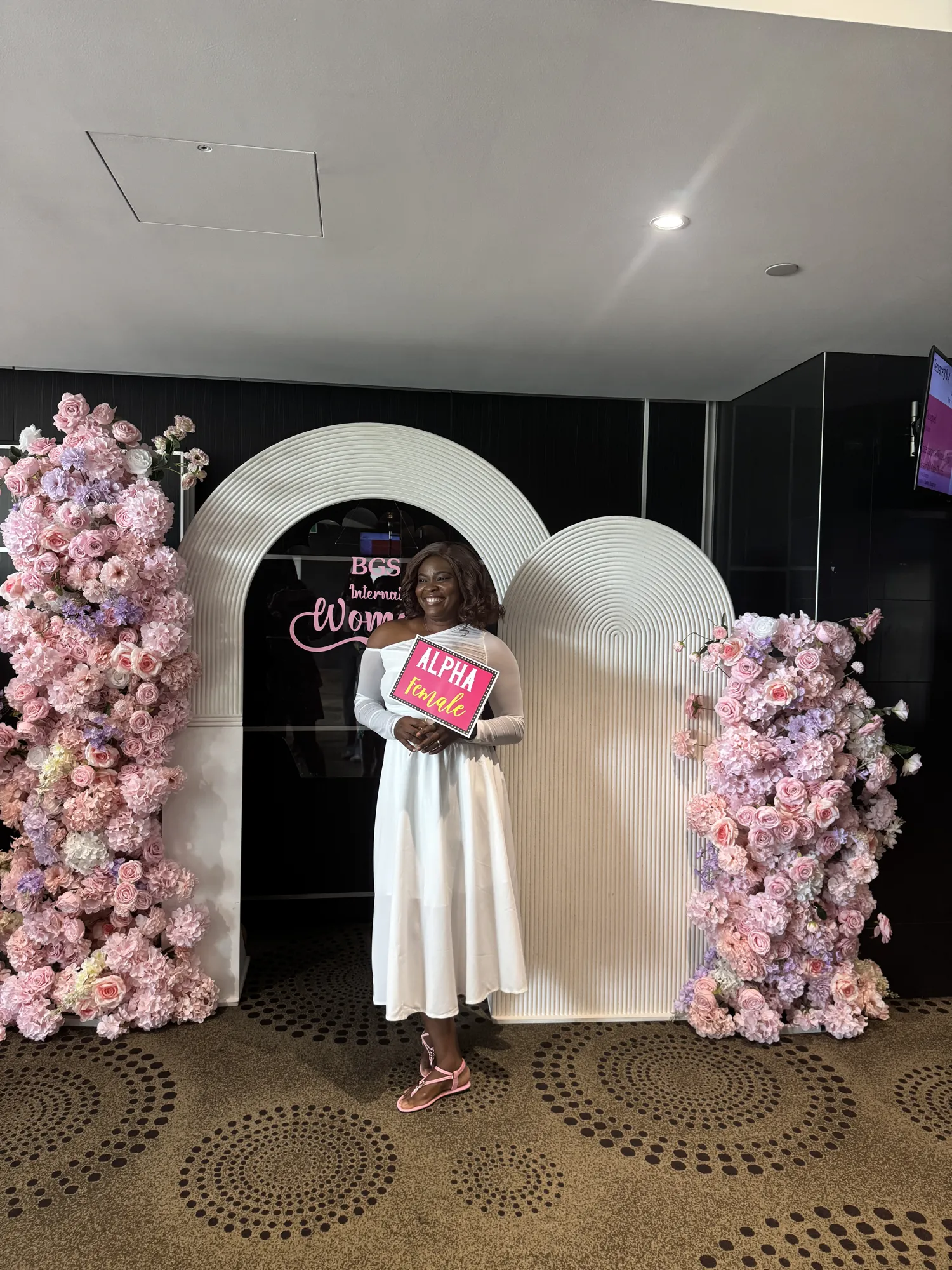A pink floral arch and a neon sign reading International Women's Day, with a small table of flowers and candles in front.