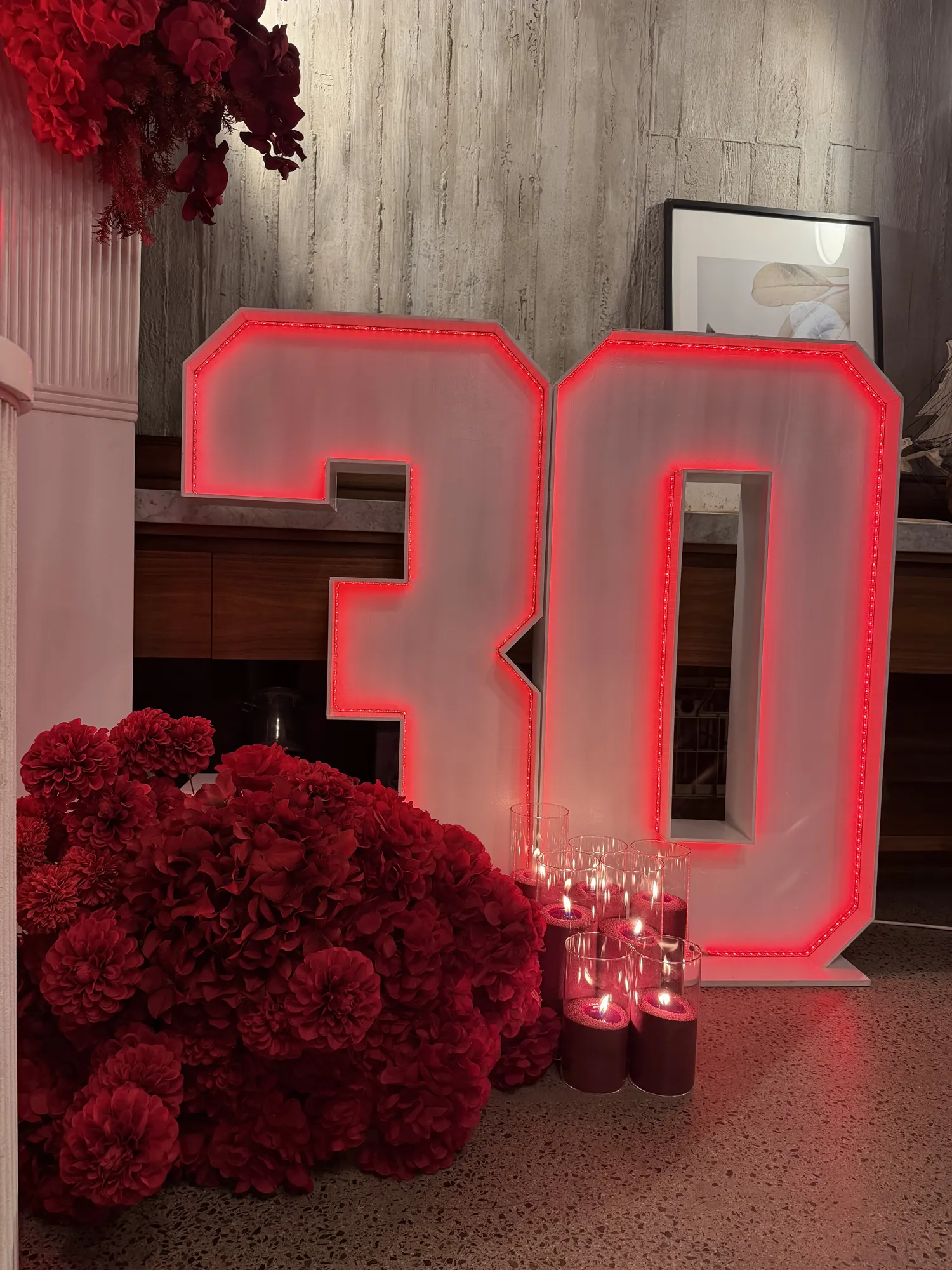 A place setting with a red napkin, gold cutlery, and a red rose, with a white arch and a marquee 30 behind.