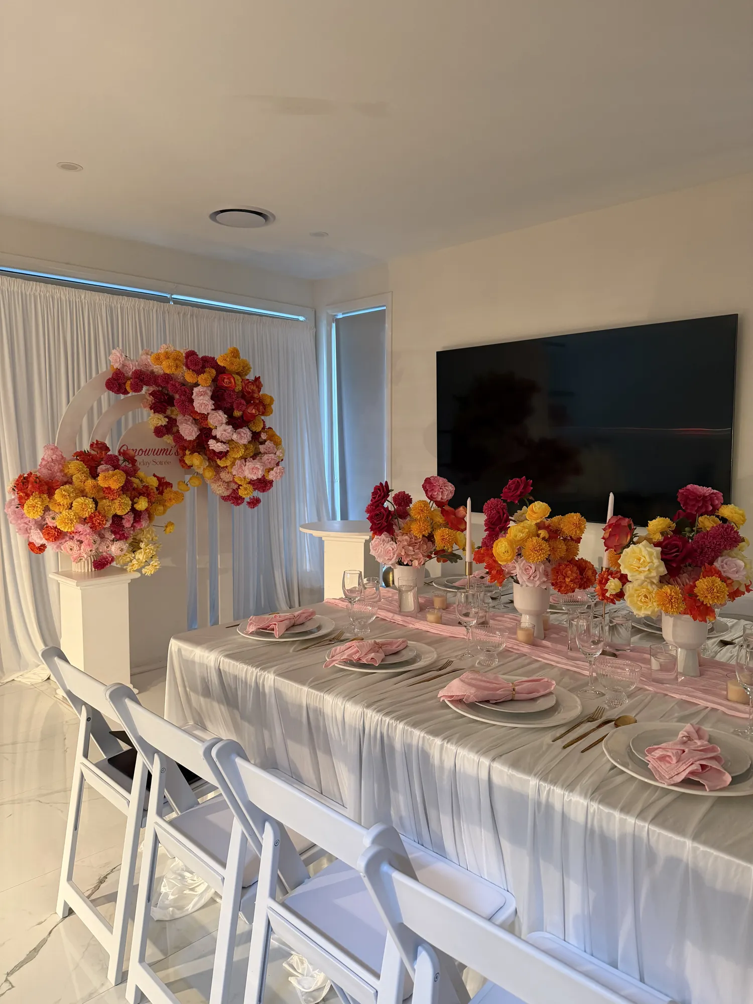A place setting with a red napkin, gold cutlery, and a low arrangement of red and white roses.