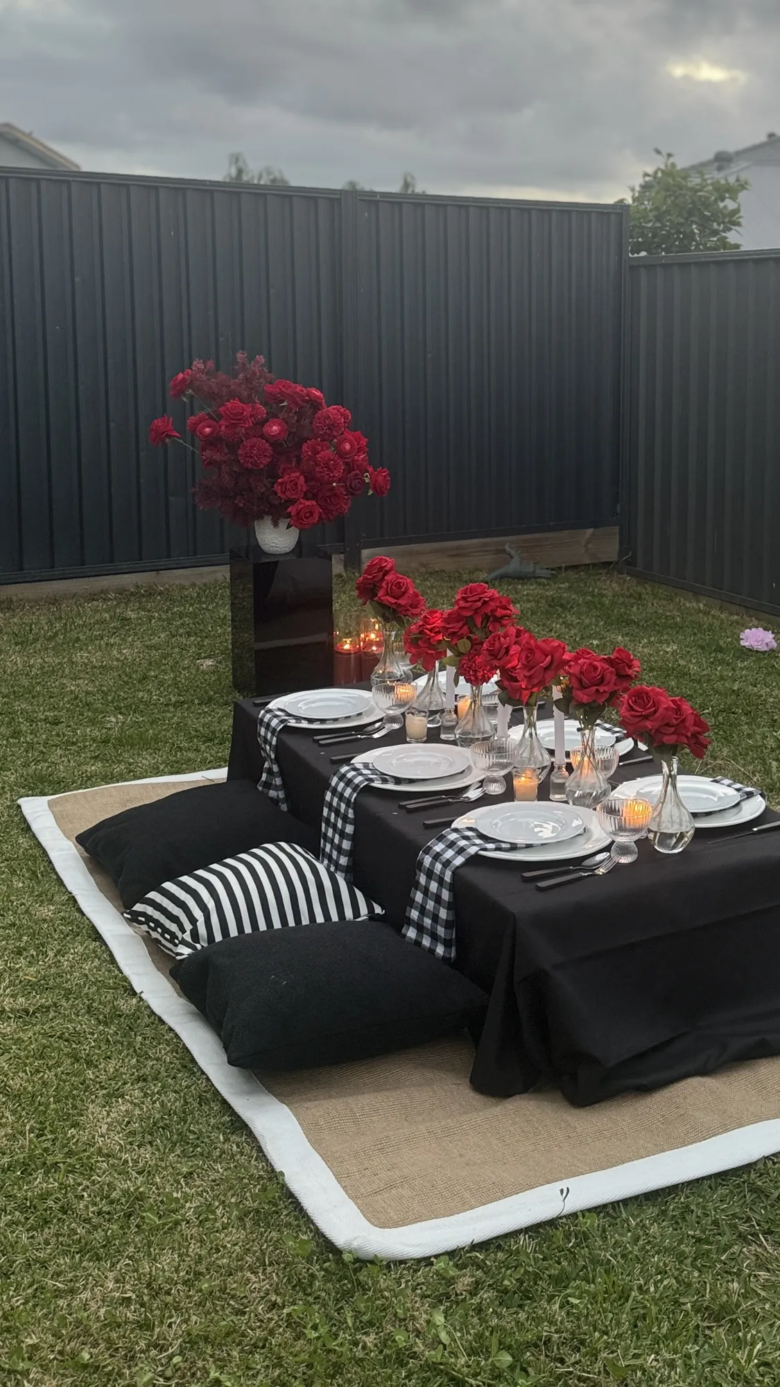 A closer view of a picnic table in white linen, with a white floral centrepiece and a tiered stand of treats.