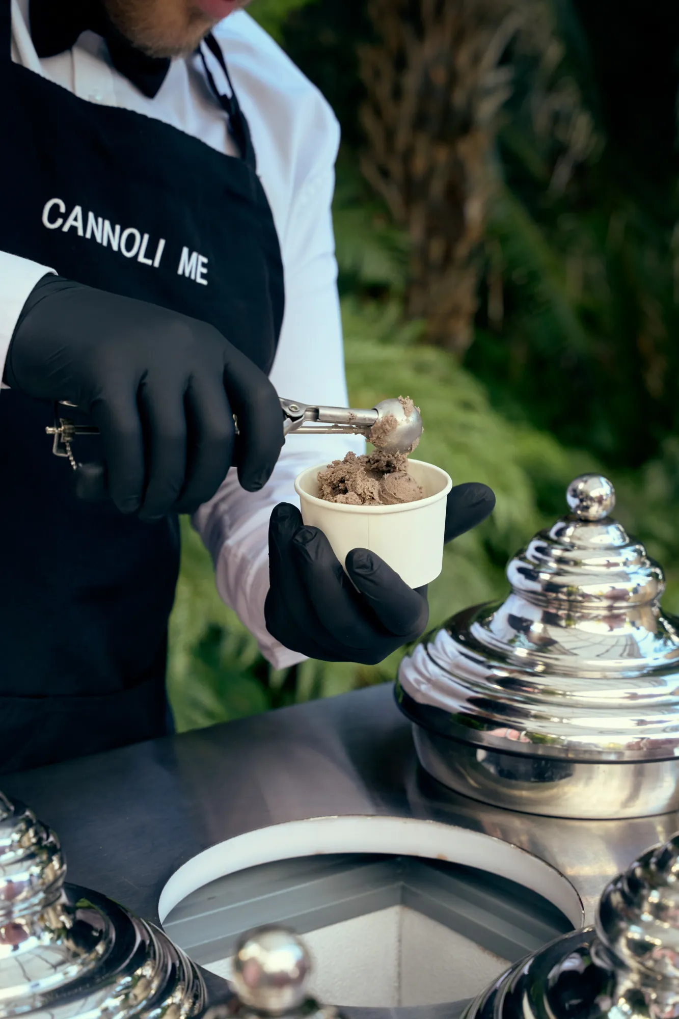 A gloved hand holding a waffle cone with a scoop of pink gelato.
