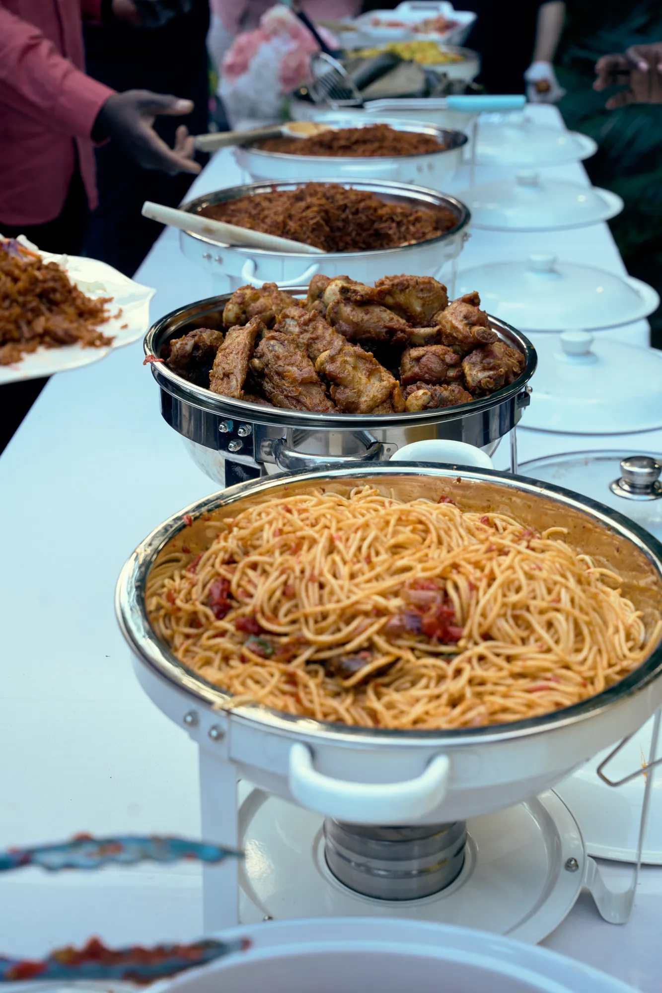A buffet of fried rice, grilled chicken, and salads on silver stands.