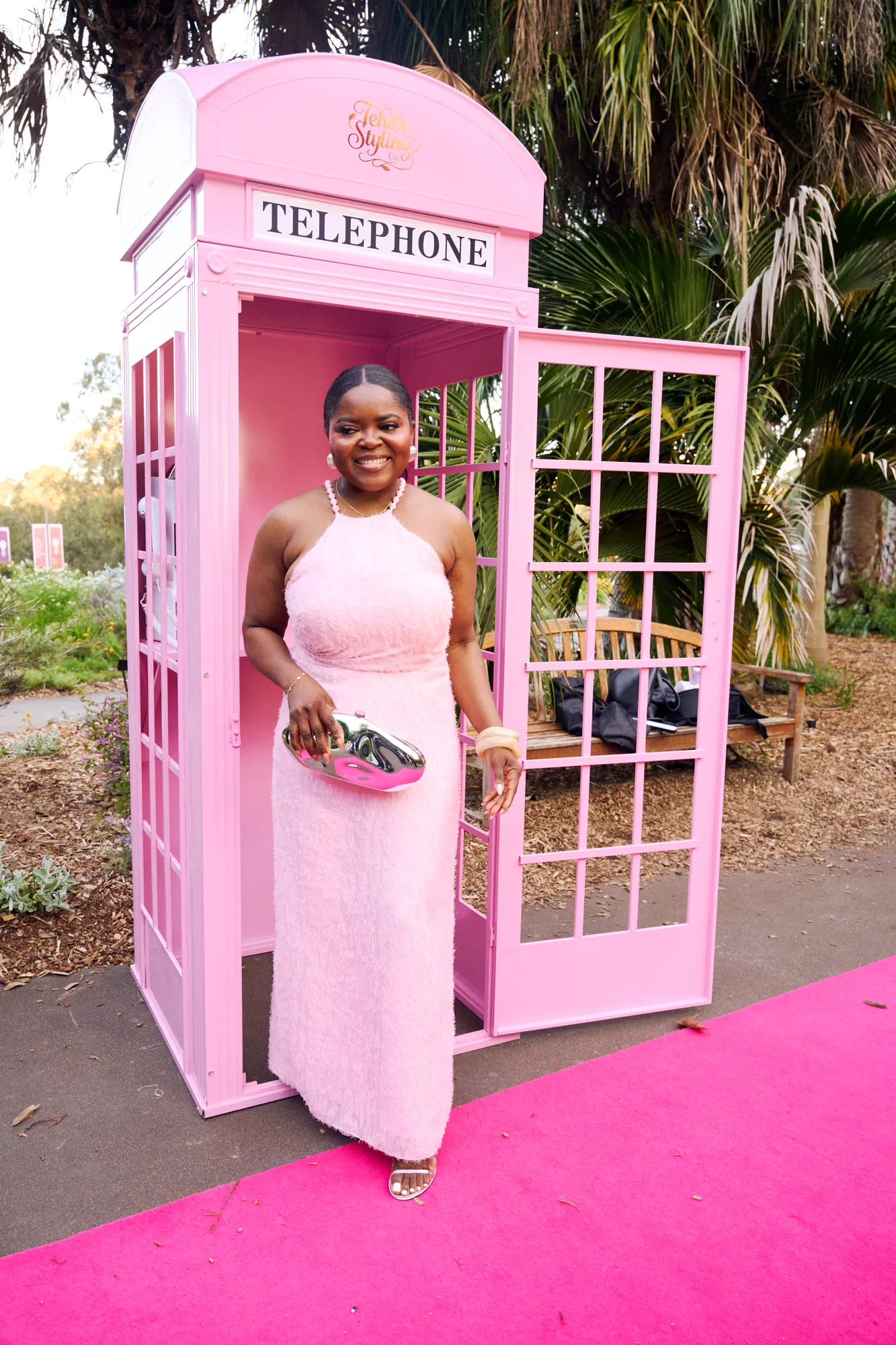 A guest inside a glossy pink telephone booth, holding the black handset to their ear.