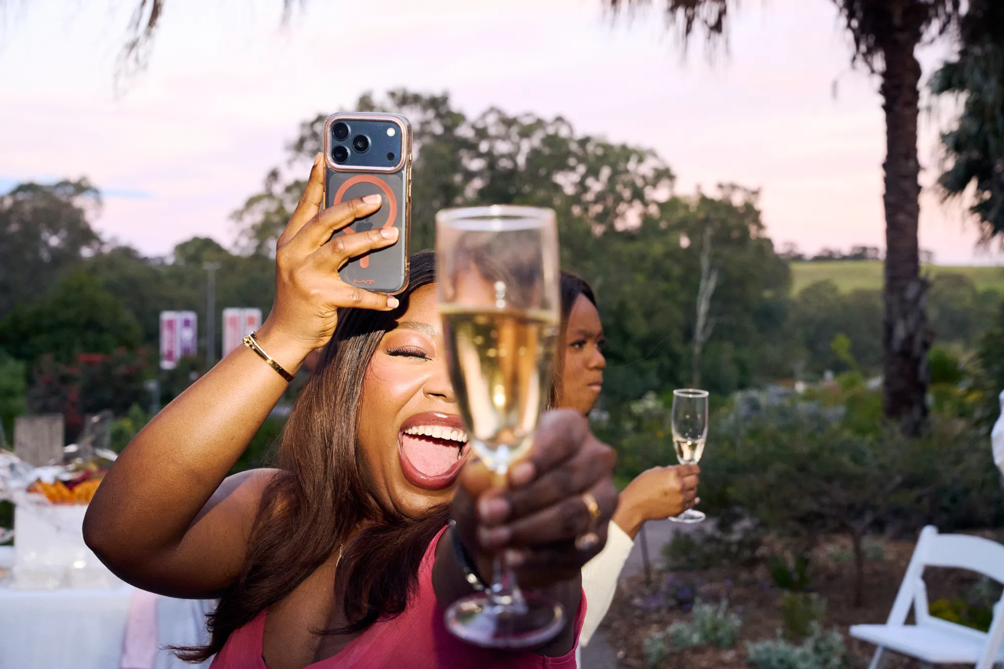 A guest raising a champagne flute in a toast beside a white floral backdrop.