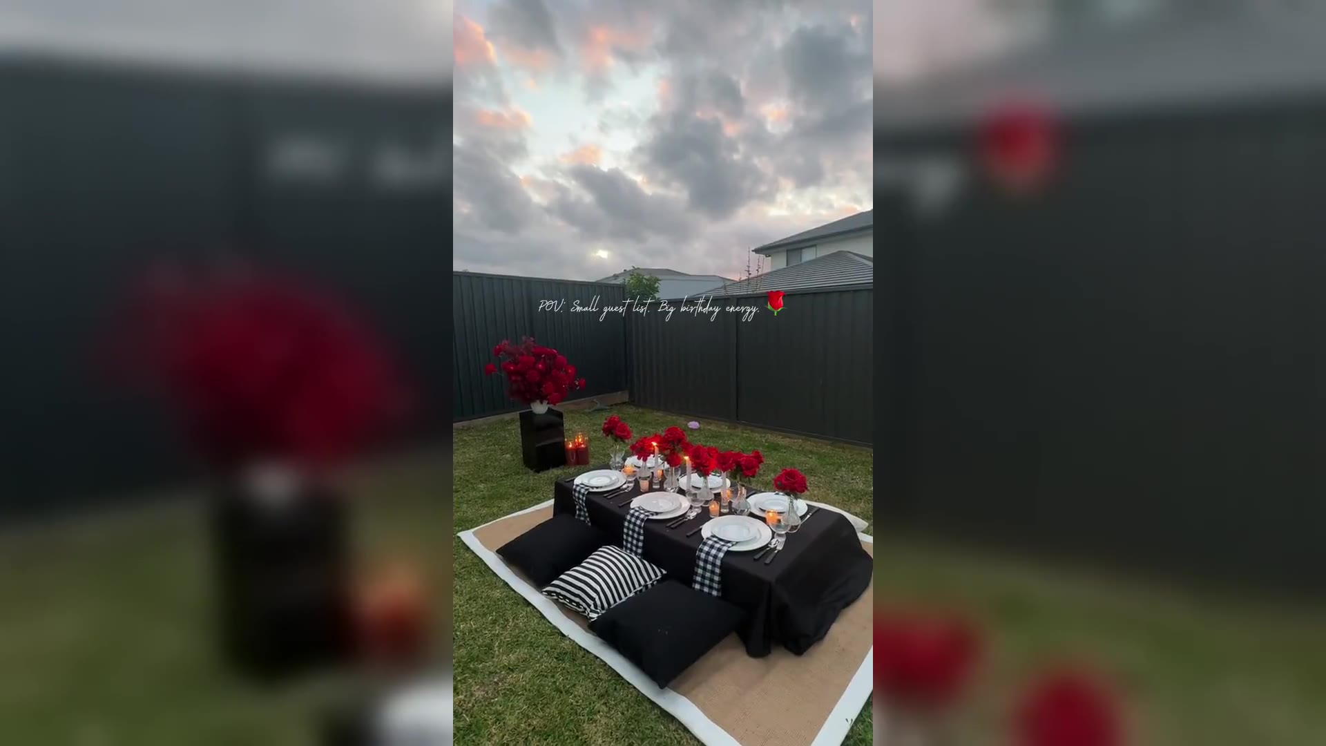 A long outdoor table in white linen with pink napkins, crystal lamps, and white and pink flowers, under a hanging floral installation.