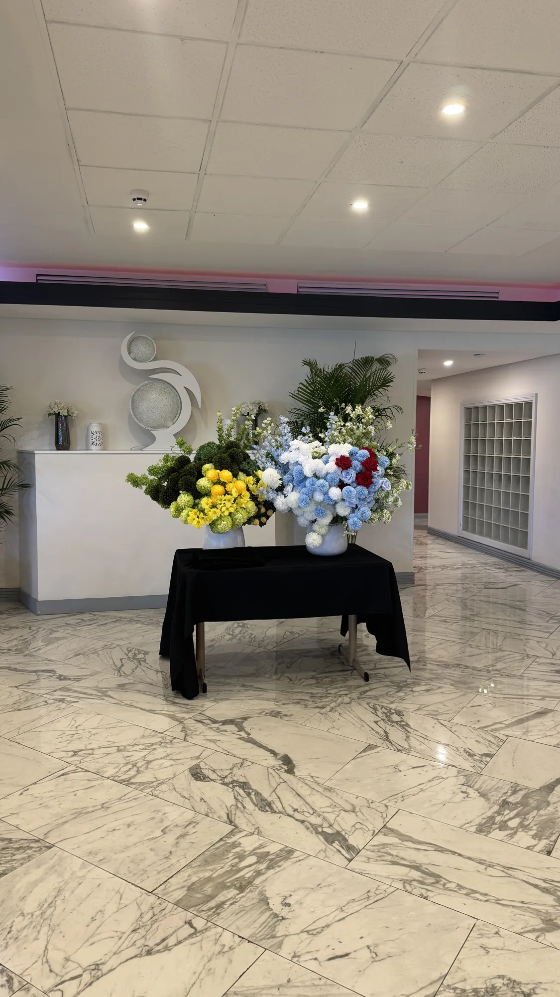 Two floral arrangements on a draped table in a marble foyer